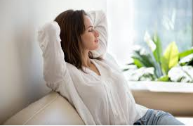 A woman sitting on a couch with her hands behind her head.