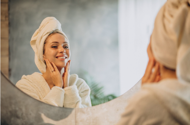 A woman in white robe looking at her reflection in mirror.