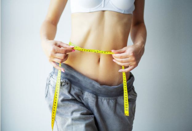 A woman is measuring her waist with a tape measure.