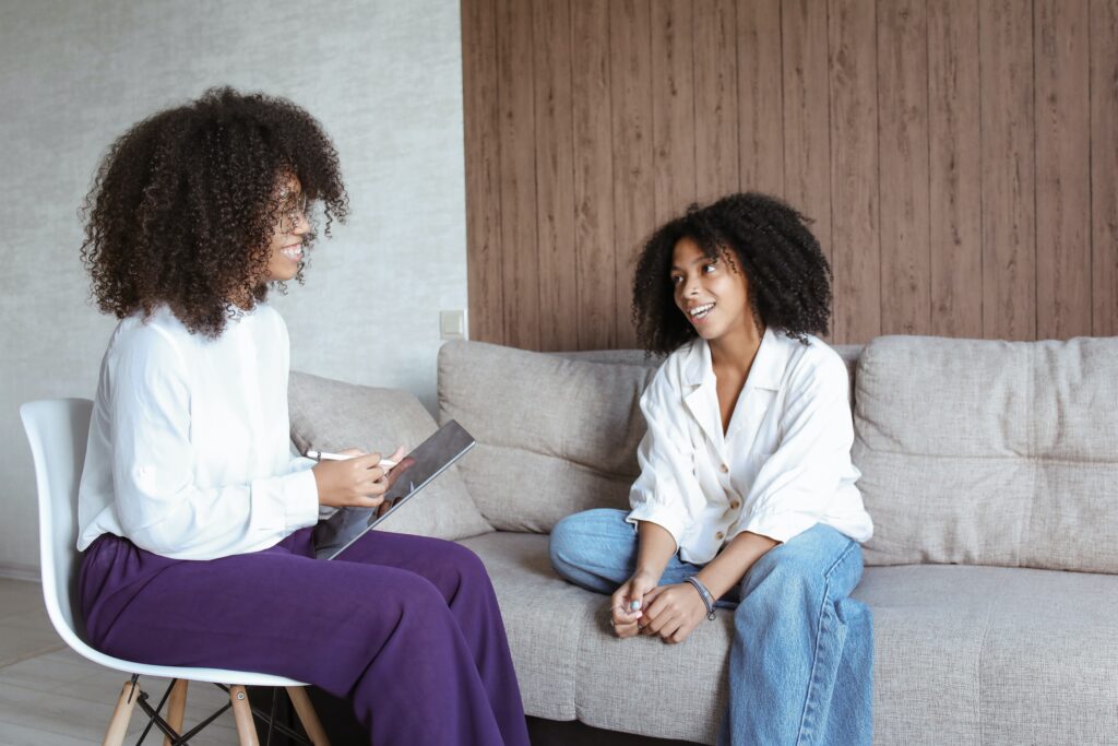 Two women sitting on a couch talking to each other.